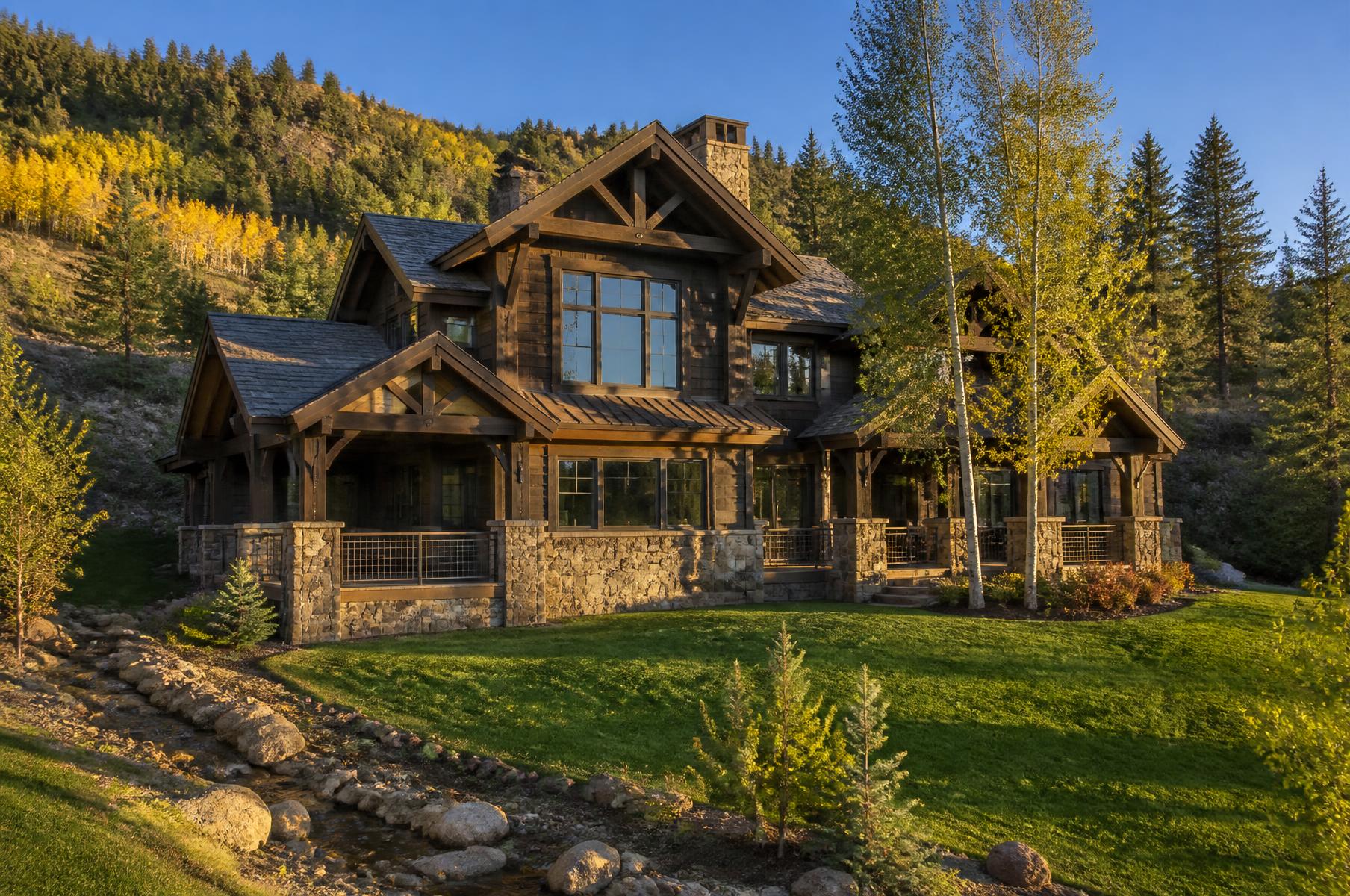 Completed rustic timber and stone home on a creek-side slope with golden fall aspens on the hillside behind
