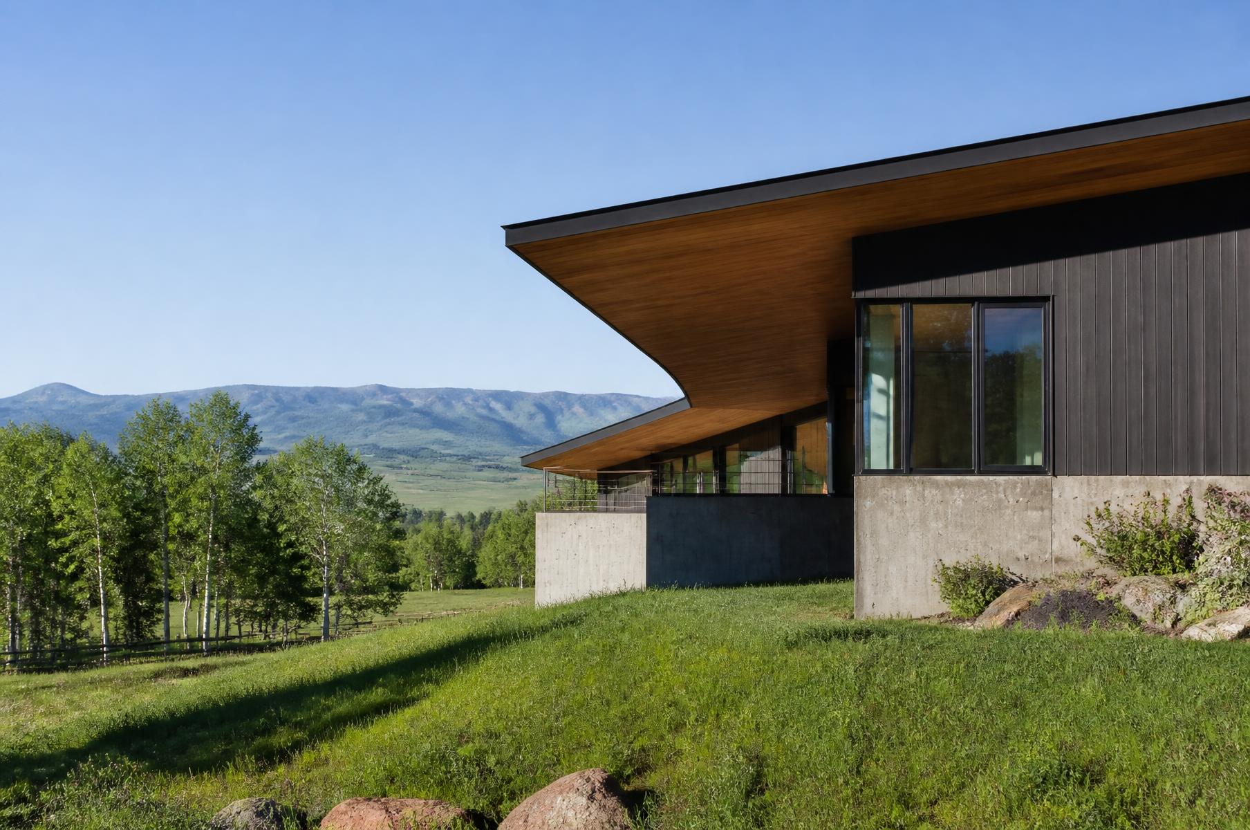 Completed mountain modern home set into a green ranch bench with a long cantilevered roof and warm wood soffit