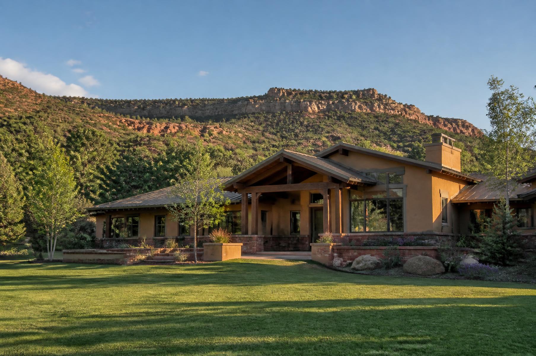 Completed southwest transitional home in earth plaster and red sandstone with a timber portal below a red rock mesa