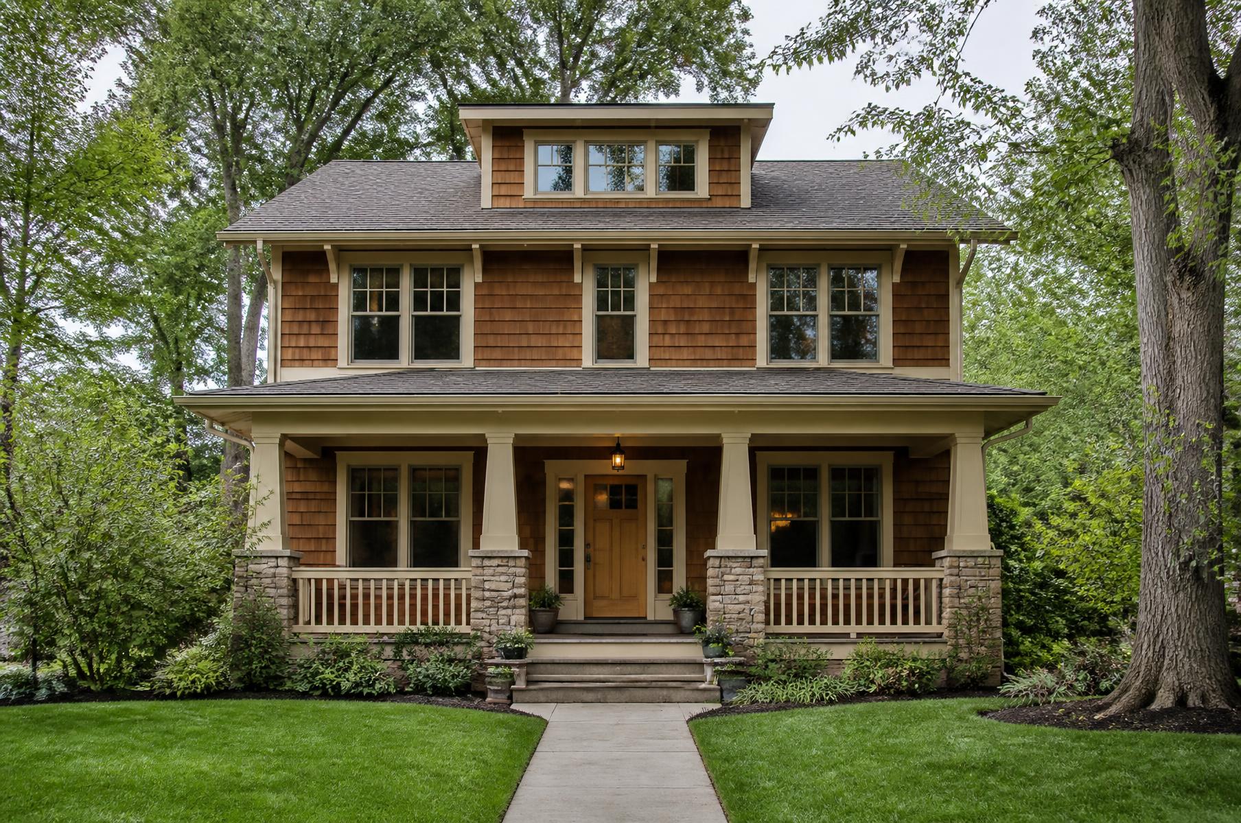 Completed two-story craftsman home with cedar shingles, cream trim and a full-width porch under mature green trees