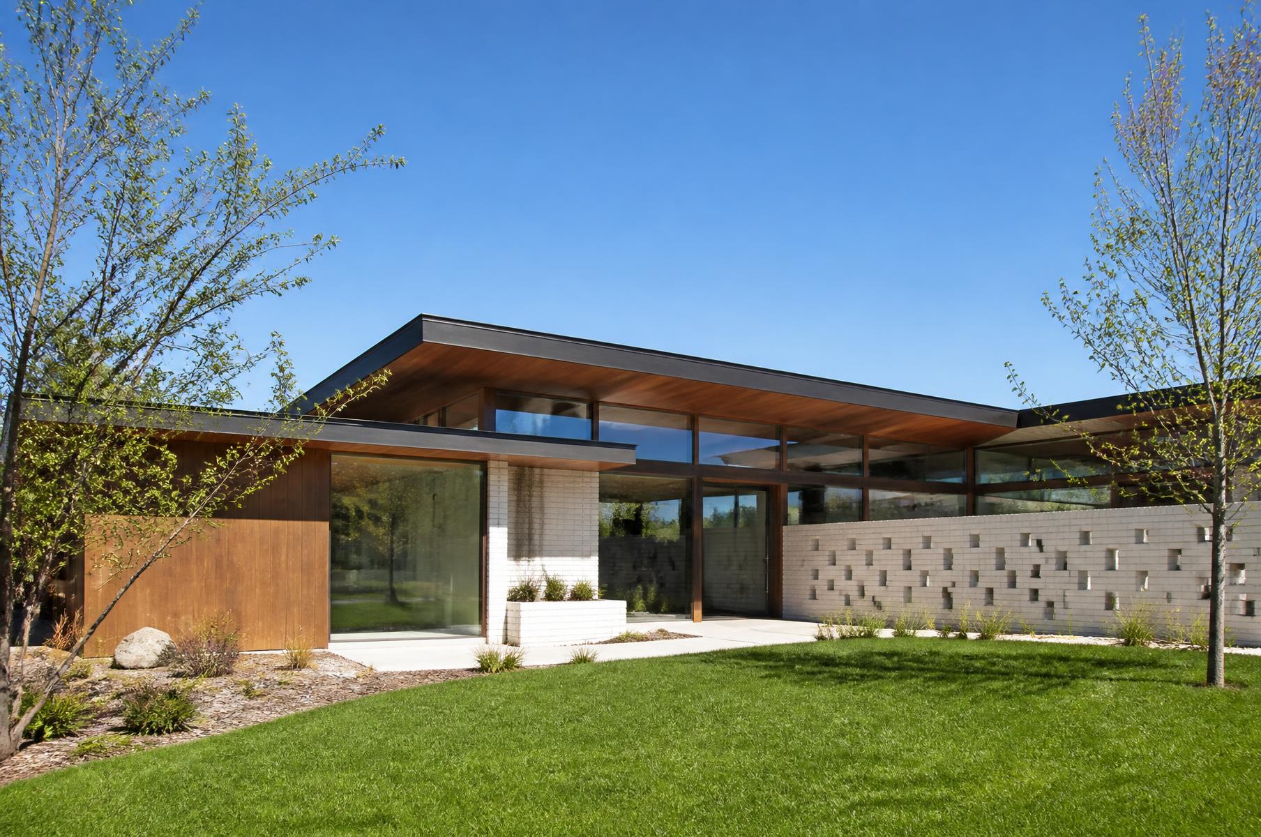 Completed mid-century inspired home with a low butterfly roof, wood panels and a white brick screen wall on a green lawn
