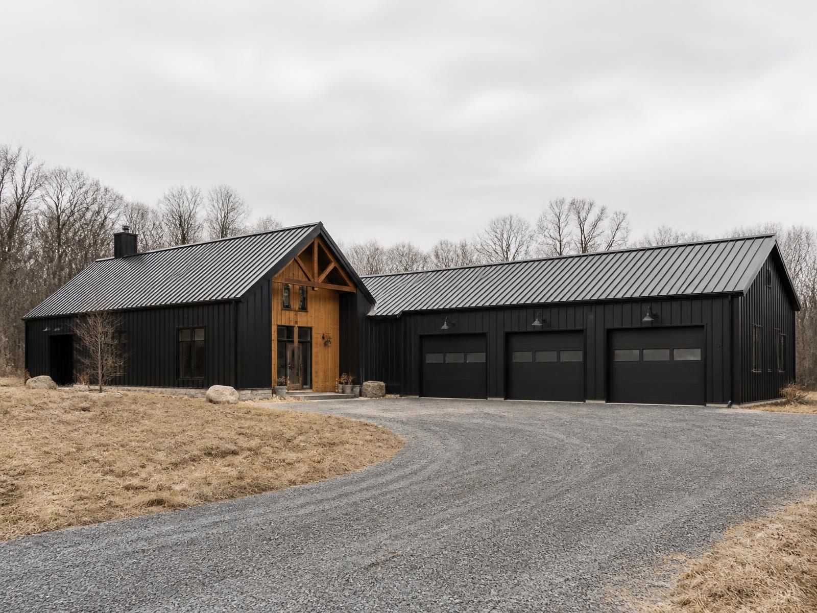 Barndominium concept in matte black steel with a warm timber entry and workshop wing on green Colorado farmland in summer