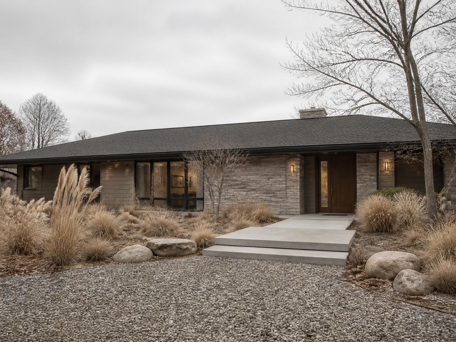 Long single-story ranch home concept with warm grey siding and a stone entry wall on a green summer lawn below the Front Range