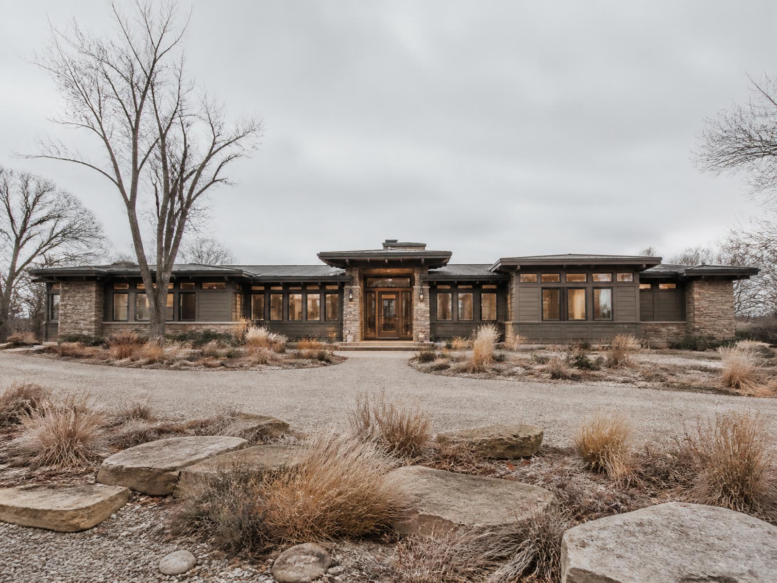 Long single-story prairie-modern home concept with deep overhangs, warm grey siding and sandstone piers under an overcast winter sky